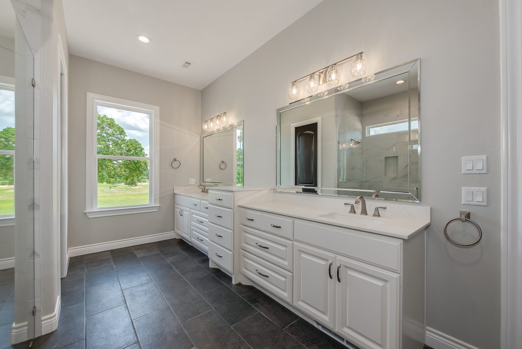 Custom home master bathroom with two sinks and dark flooring accent.